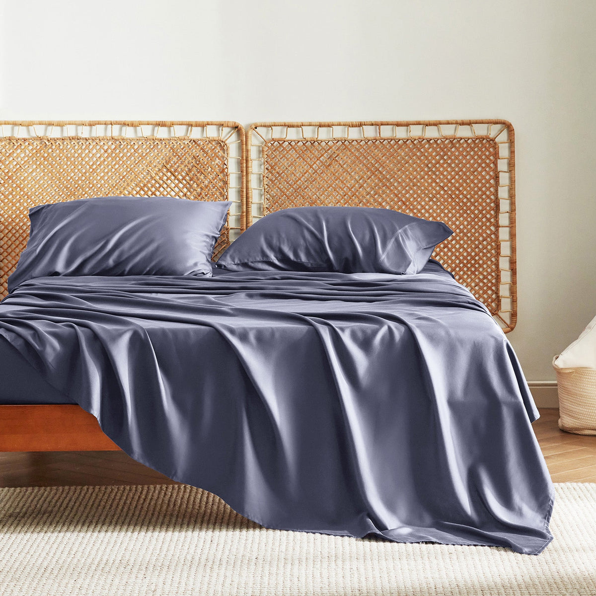Dark gray bamboo derived rayon cooling sheet set with two pillowcases elegantly draped on a bed with a rattan headboard.